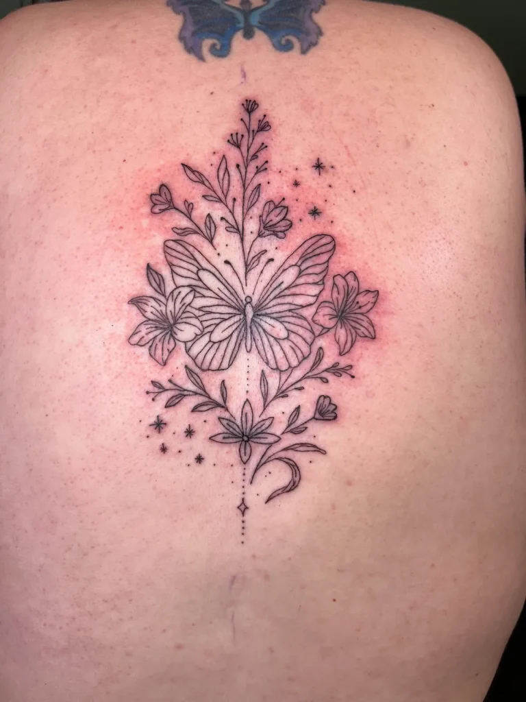 fine line back tattoo of a butterfly surrounded with lilies, botanicals, and delicate stars
